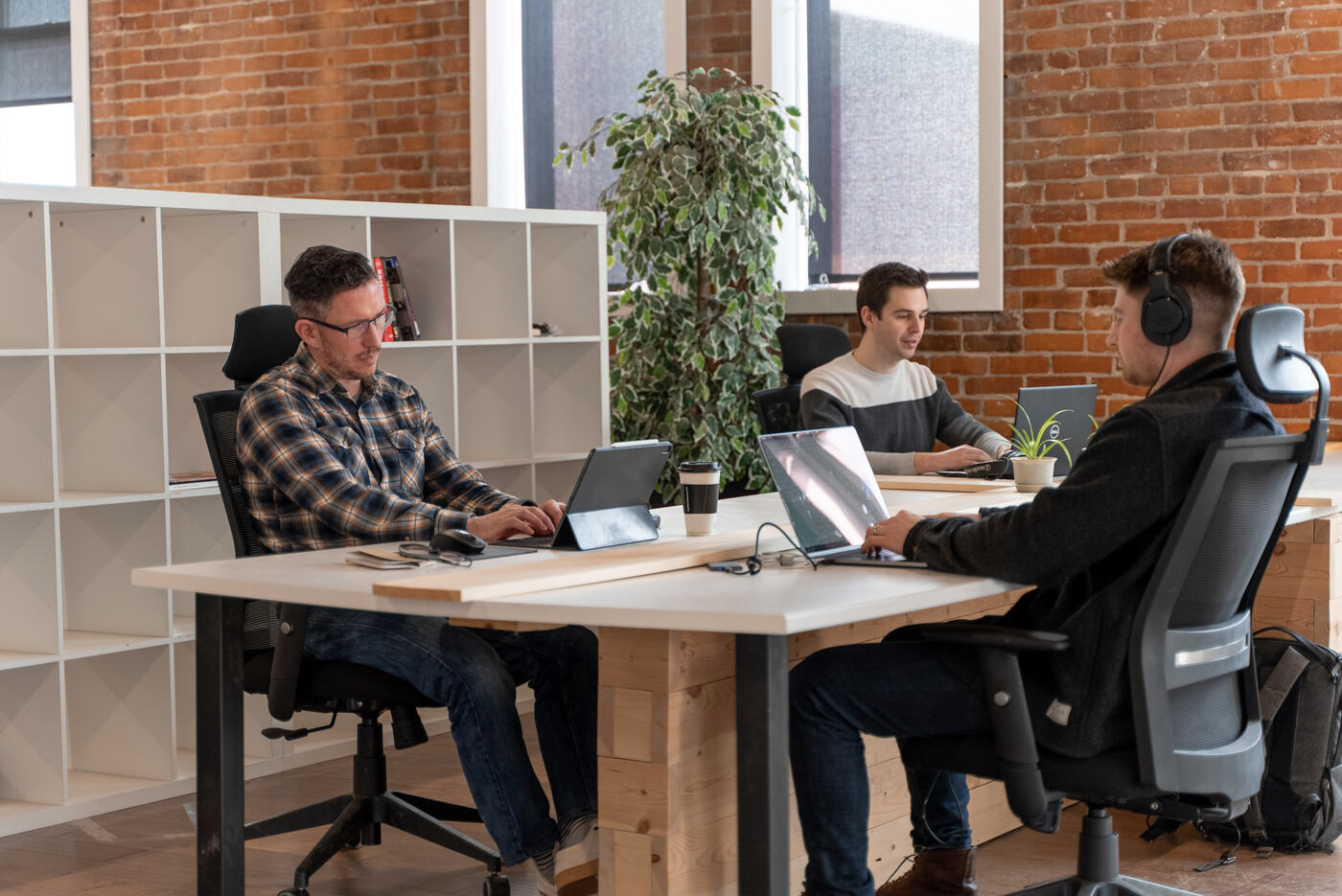 Members working at shared desks by the brick wall and windows at Altspace